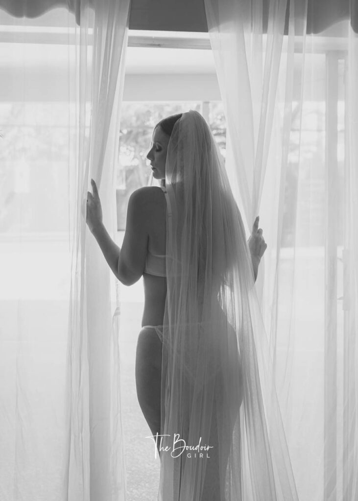 A bride to be standing at the window with her back to the photographer.